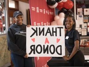 Two female students hold a poster with thank a donor written on it